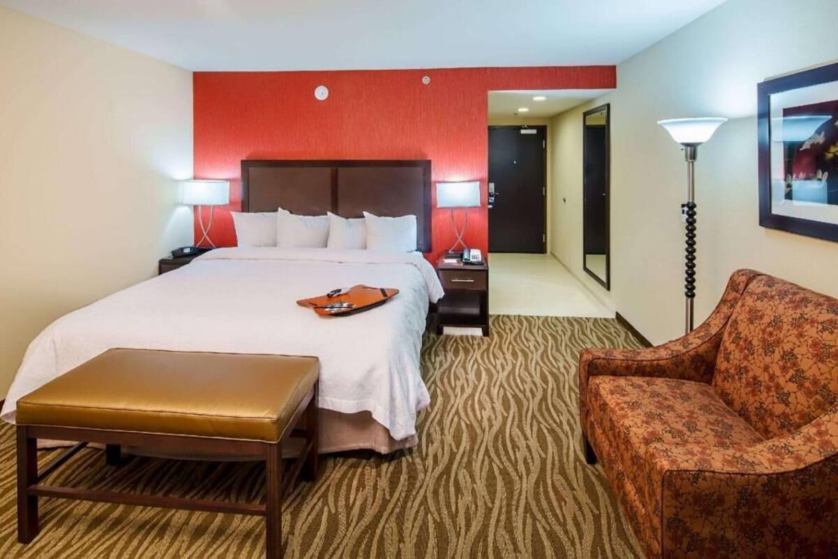 A hotel room with a bed, bedside tables, a chair, a lamp, and a carpeted floor.