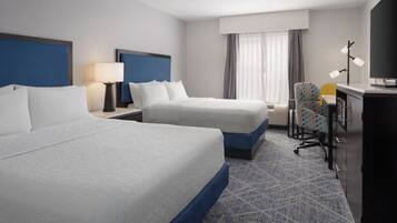 A hotel room with two beds, a desk, a chair, and a television.