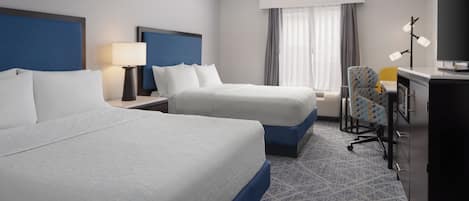 A hotel room with two beds, a desk, a chair, and a television.