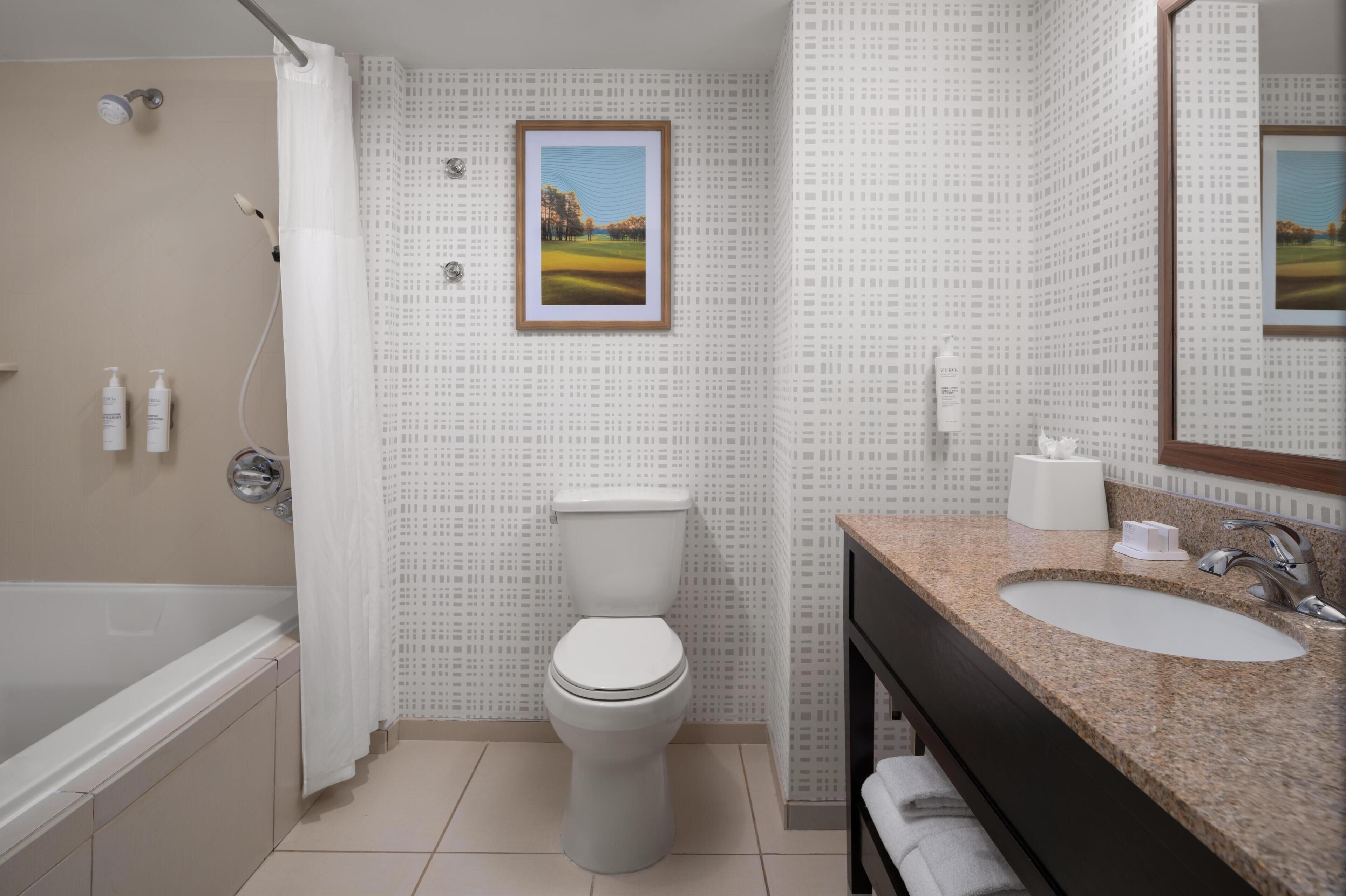 Un baño con inodoro, ducha, lavamanos y un cuadro en la pared.