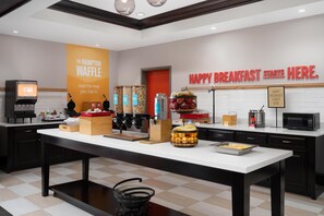 Montaje de un bufé de desayuno con una máquina de café, estación de gofres y diversos recipientes de comida.