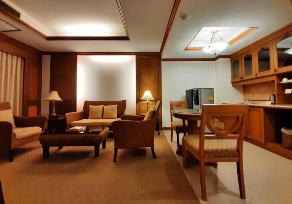 Una sala de estar acogedora con un sofá, sillones y una mesa de centro. Hay una mesa de comedor con sillas y una zona de cocina con armarios y un refrigerador.