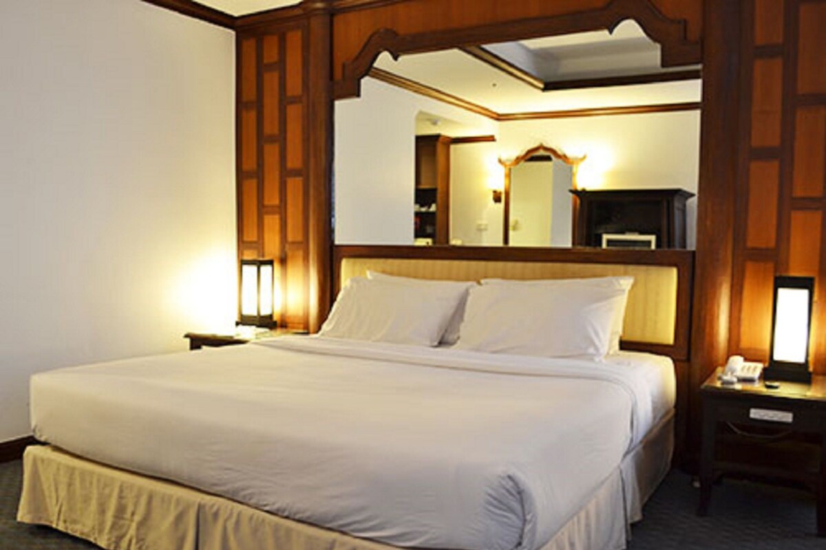 Una camera d'albergo con un letto grande, una testiera in legno, un comodino, uno specchio e una lampada.