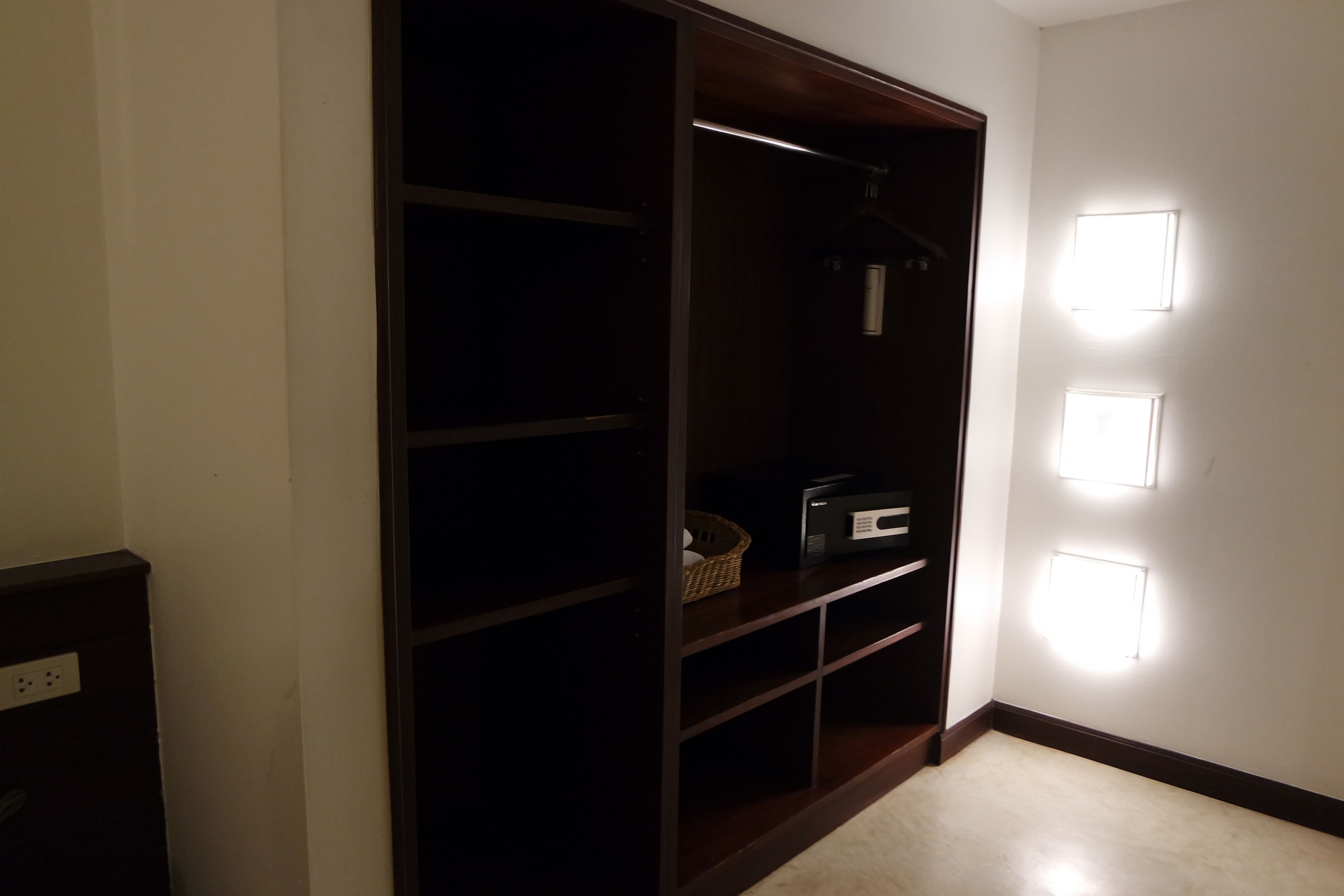 A hallway with a wooden closet, a basket, and a radio. There are wall-mounted lights on the right.