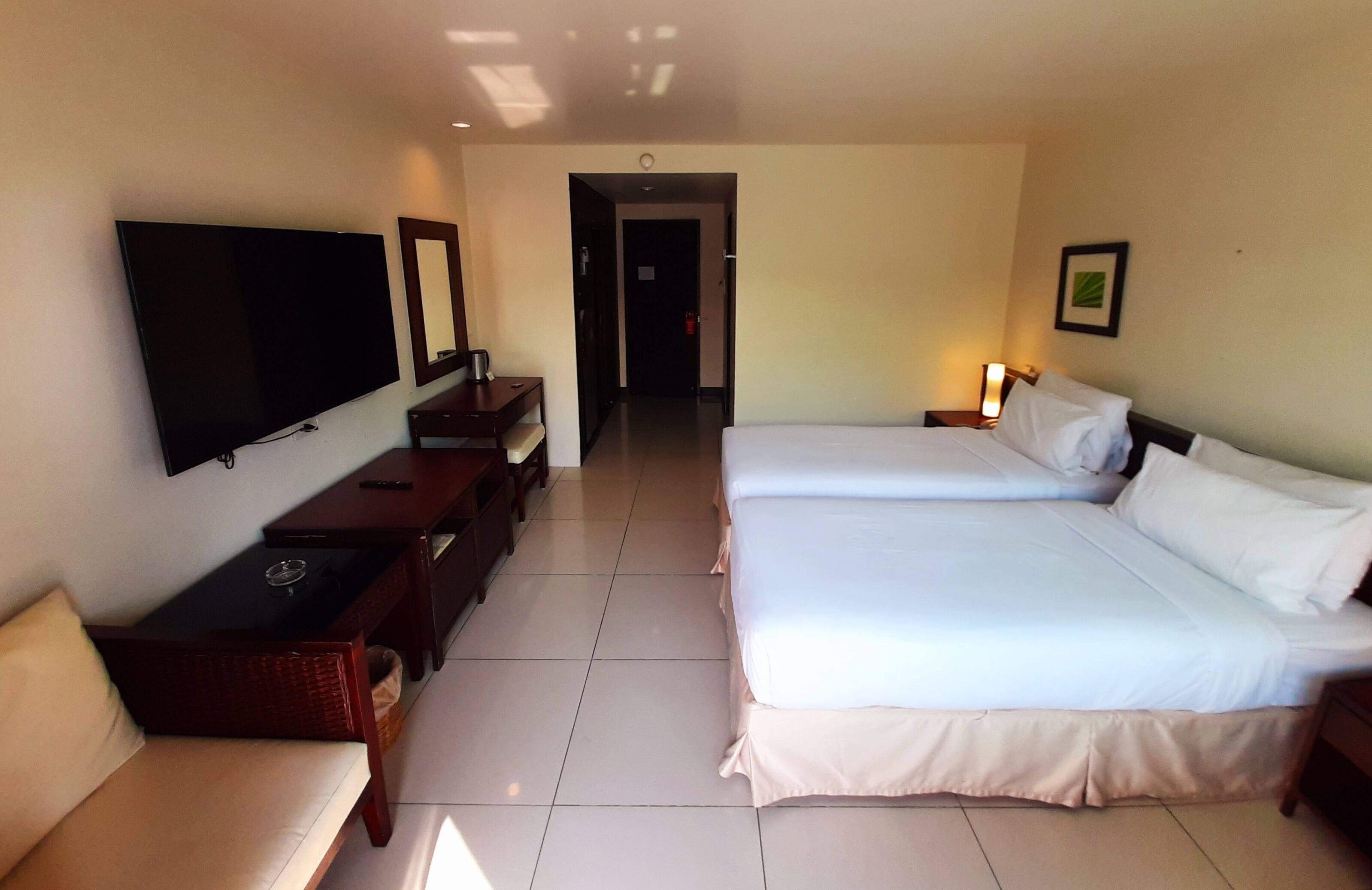 A hotel room with a large bed, a TV mounted on the wall, a desk with a chair, and a small table.