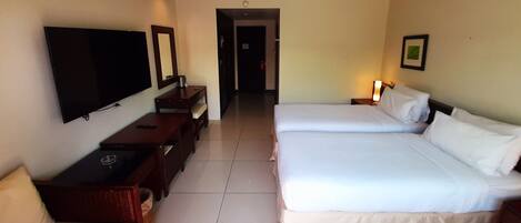 A hotel room with a large bed, a TV mounted on the wall, a desk with a chair, and a small table.