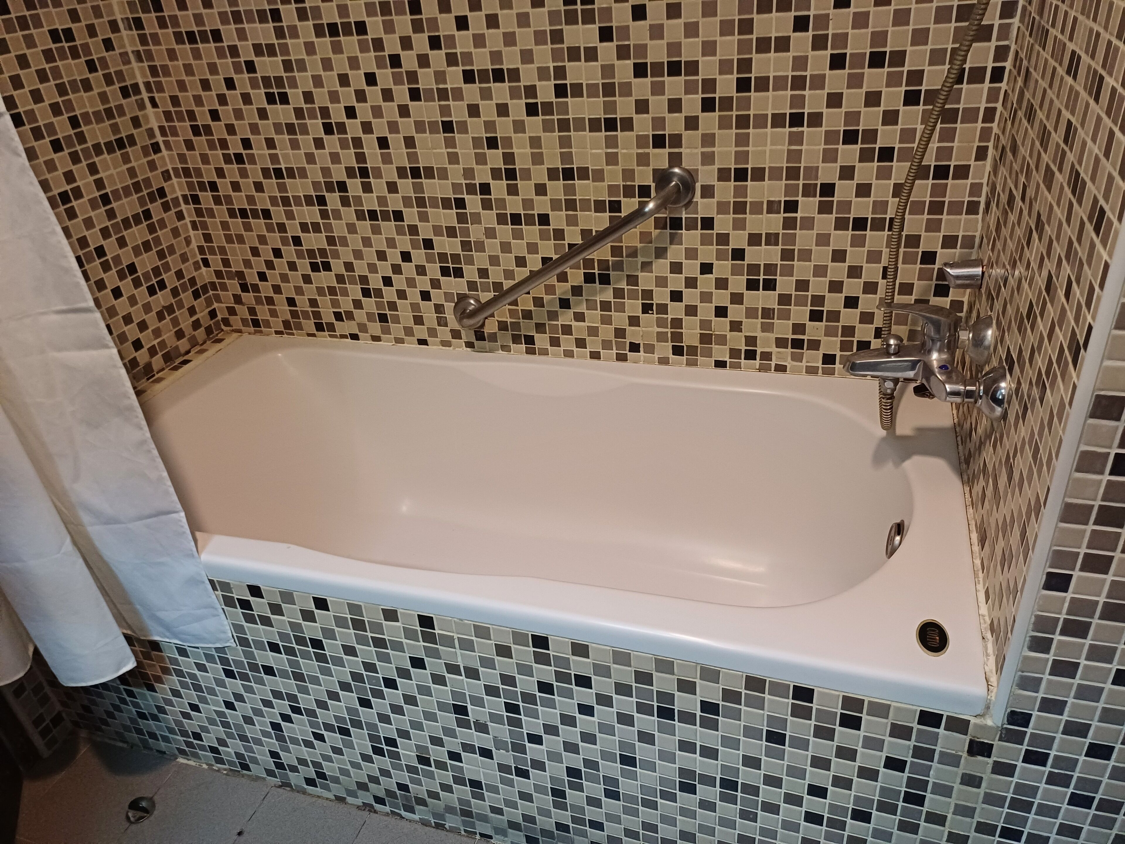 A standard bathtub with a chrome faucet and a handheld showerhead, set against a mosaic tile wall.