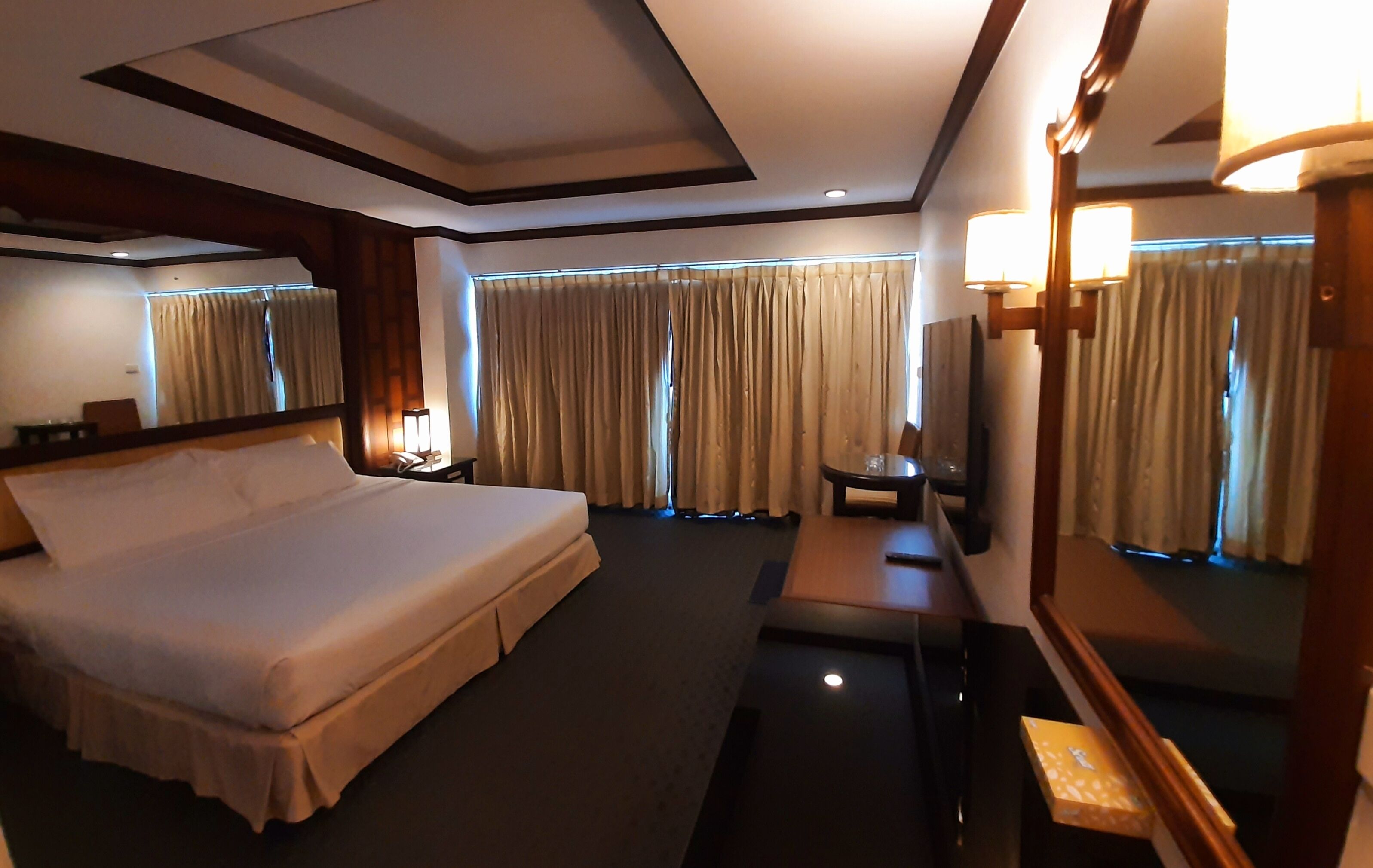 A hotel room with a large bed, a desk, a chair, a mirror, and curtains.