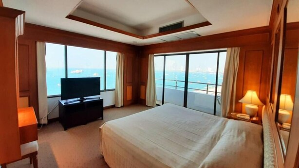 A hotel room with a large bed, a television, a desk, and a view of the sea. - Grand Hotel (Pattaya)