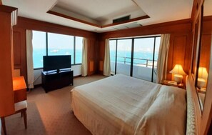 A hotel room with a large bed, a television, a desk, and a view of the sea. - Grand Hotel (Pattaya)