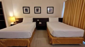 A hotel room with two beds, a nightstand with a lamp, and three framed pictures on the wall.