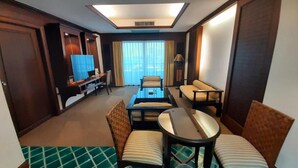 A hotel room with a seating area featuring a sofa, a small table, and two chairs. There is a television and a window with curtains. - Grand Hotel (Pattaya)