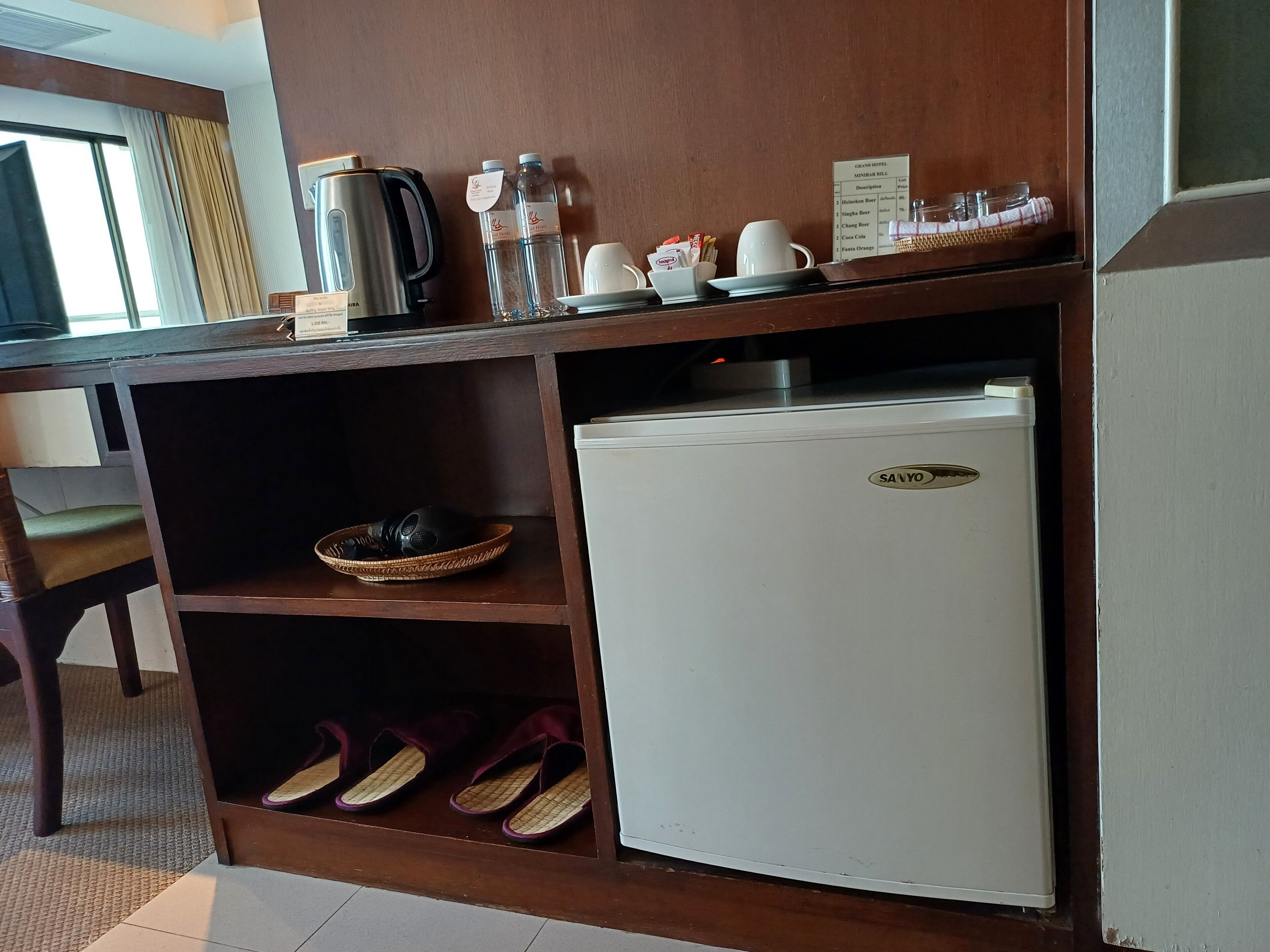 Eine kleine Küchenzeile mit Kaffeemaschine, Wasserflaschen und Kühlschrank.