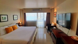 A hotel room with a large bed, a desk with a television, and a window with curtains. - Grand Hotel (Pattaya)
