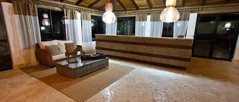 Een ruime woonkamer met een houten plafond, een zithoek, een salontafel en twee hangende hanglampen.