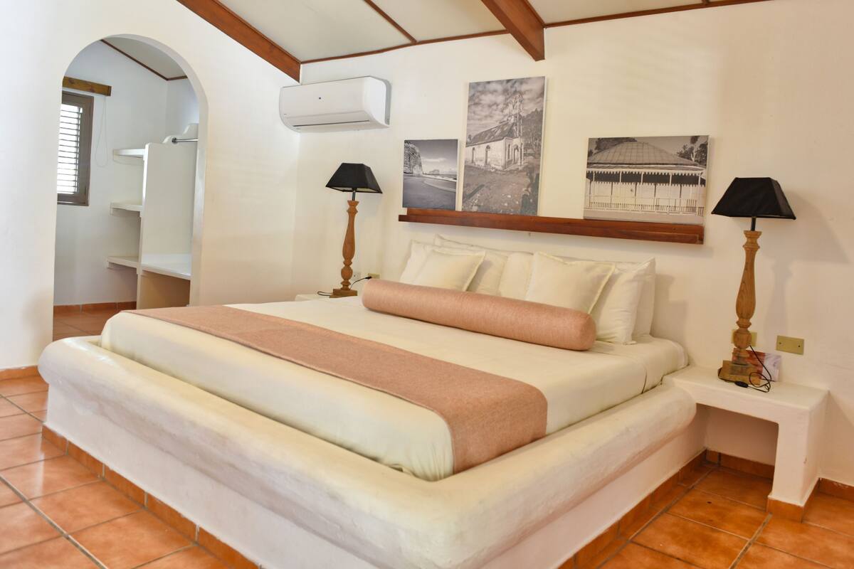 A bedroom with a large bed, two bedside lamps, a nightstand, and a wall-mounted air conditioner.