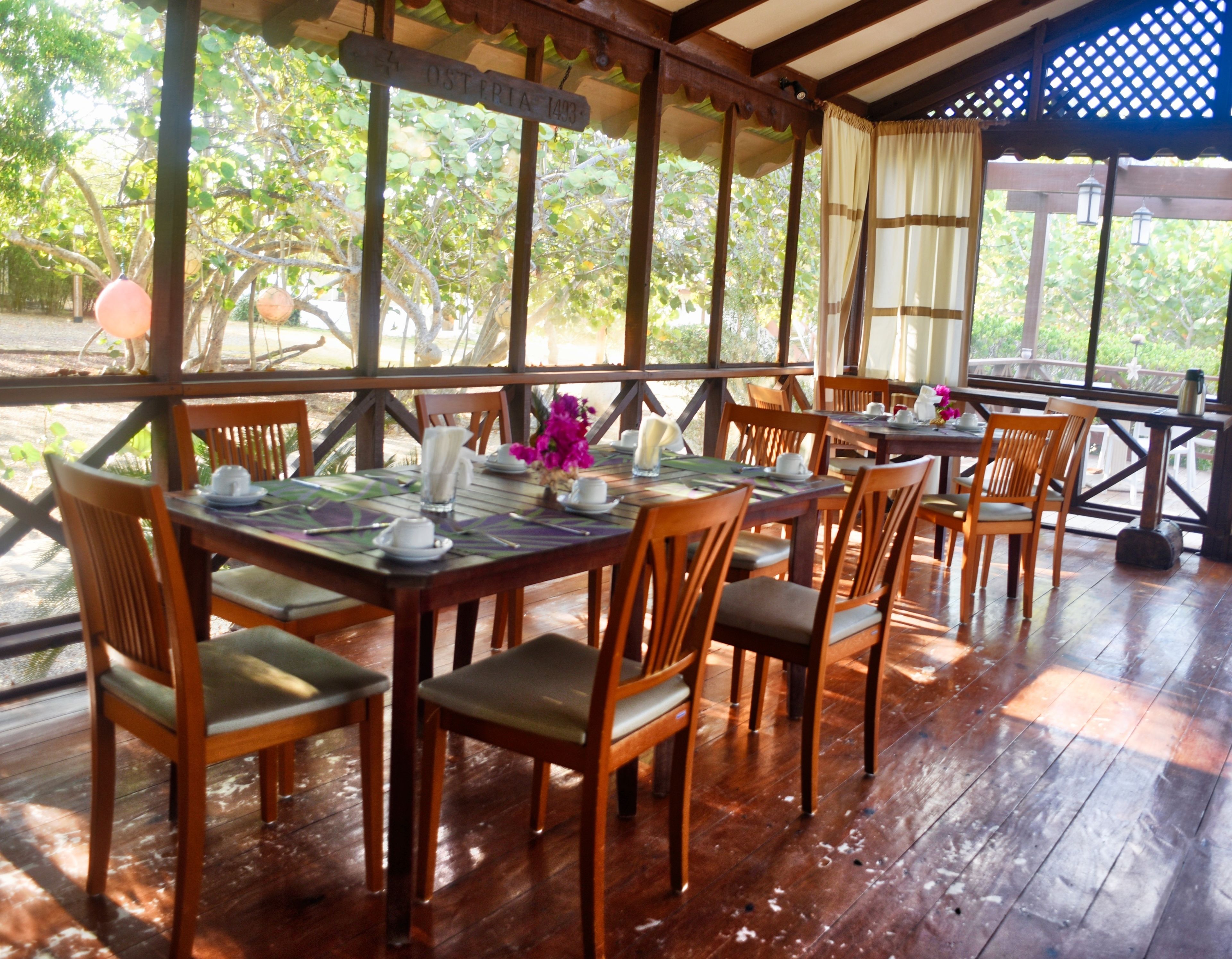 Een restaurant met houten tafels en stoelen, terras en uitzicht op groen.