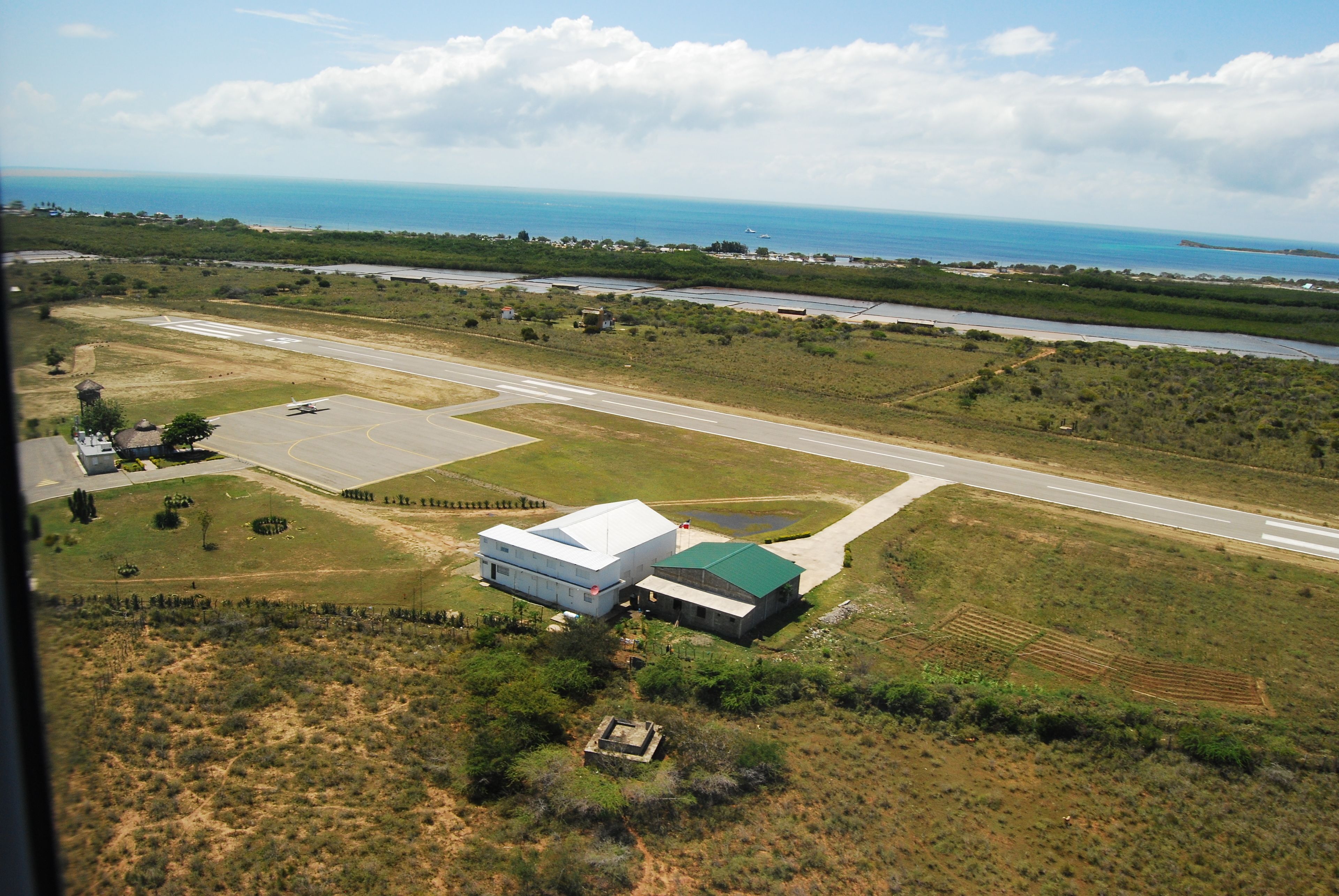 An aerial view of a coastal area with a runway, buildings, and a body of water.