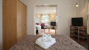 A hotel room with a bed, a wardrobe, a television on a stand, and a view into the living area. - Dorset Hotel (Ryde)