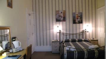 A bedroom with a bed, a desk with a chair, a lamp, and a painting on the wall.