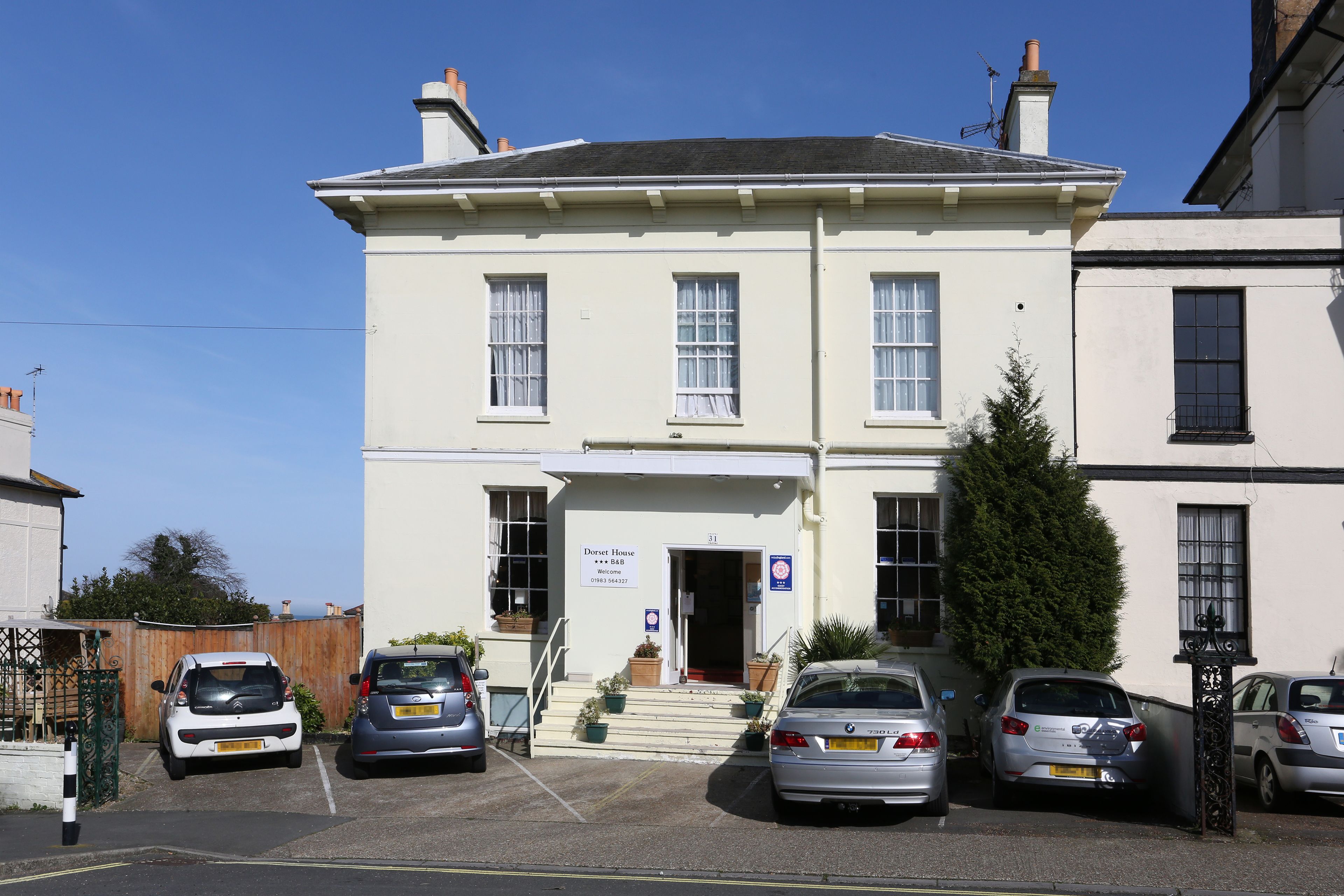 A two-story building with a sign reading "Dorset House" and a parking area with several cars.