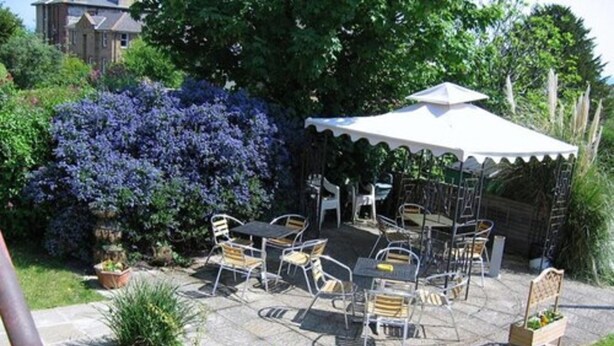 An outdoor patio with a table and chairs, surrounded by potted plants and a large bush. - Dorset Hotel (Ryde)