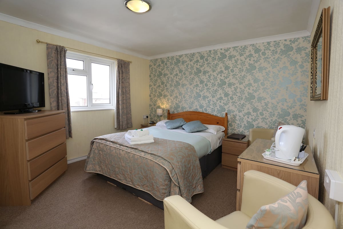 A hotel room with a bed, a television, a desk with a coffee maker, and a chair.