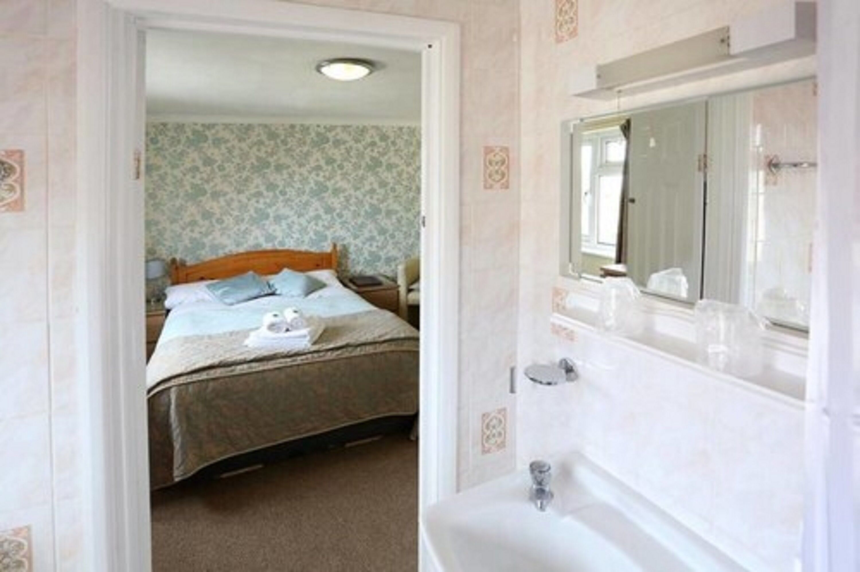 Un dormitorio con una cama, una mesita de noche y una mesa auxiliar. Hay un baño con un lavamanos y un espejo.