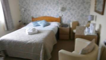 Una habitación de hotel con una cama, una silla, una mesita de noche y una mesita auxiliar.