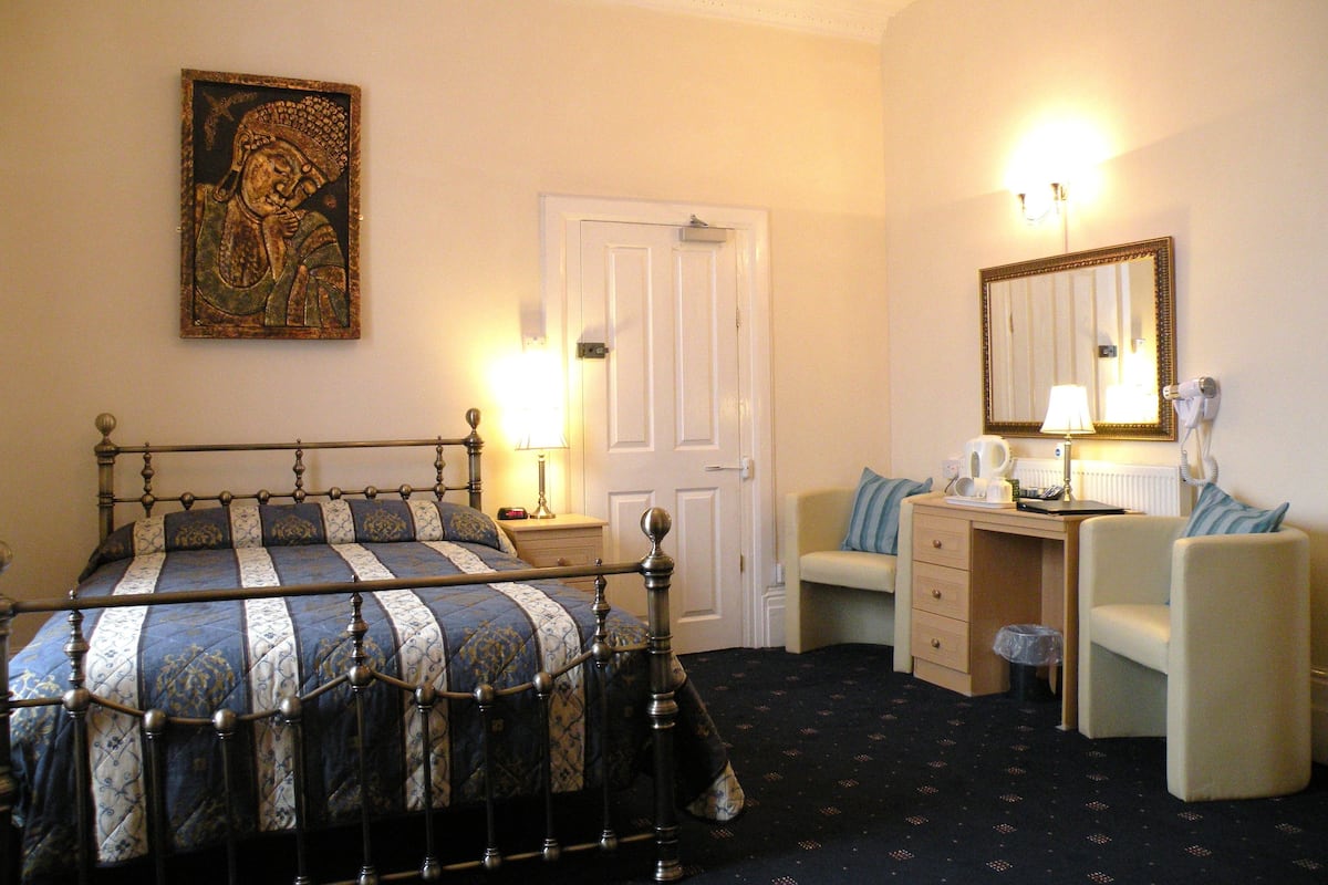 A bedroom with a bed, a desk, a chair, a mirror, and a door.