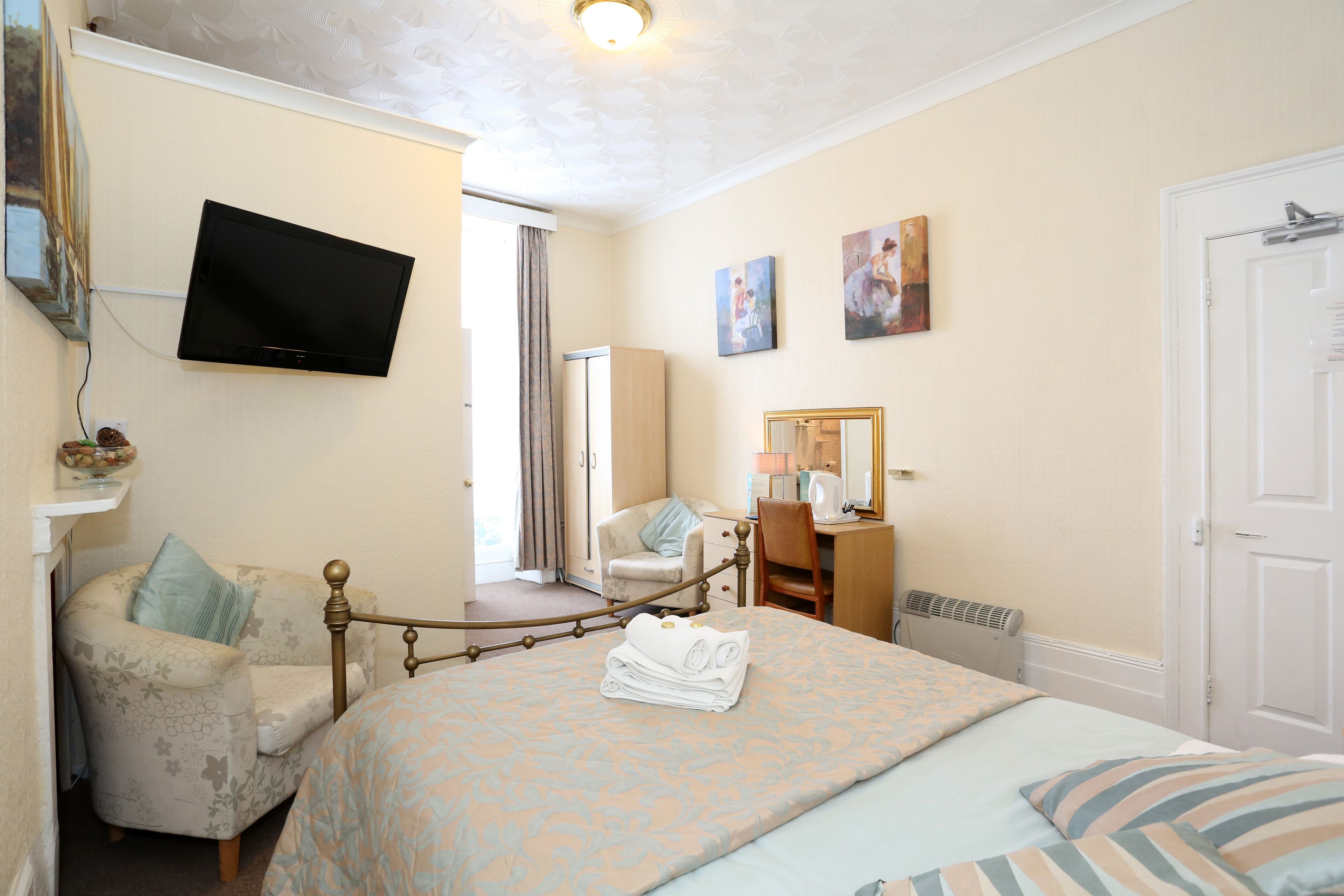Una habitación de hotel con una cama, una silla, un escritorio, un televisor y obras de arte en las paredes.