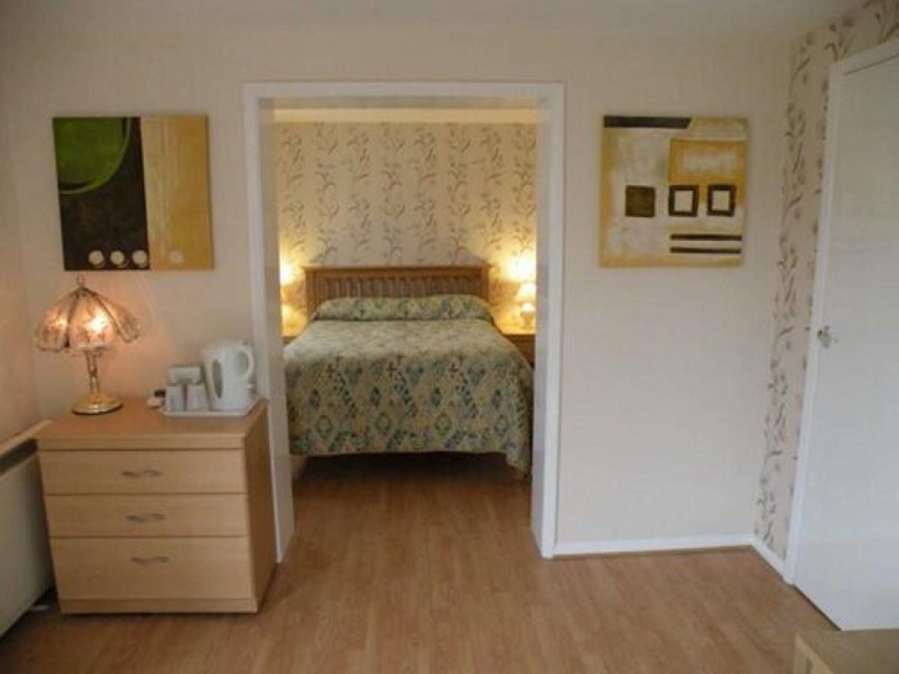Un dormitorio con una cama, una mesita de noche con lámpara y un aparador.
