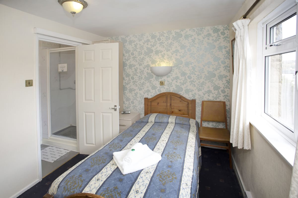 A bedroom with a bed, a wooden headboard, a nightstand, a wall-mounted light, and a window with curtains.