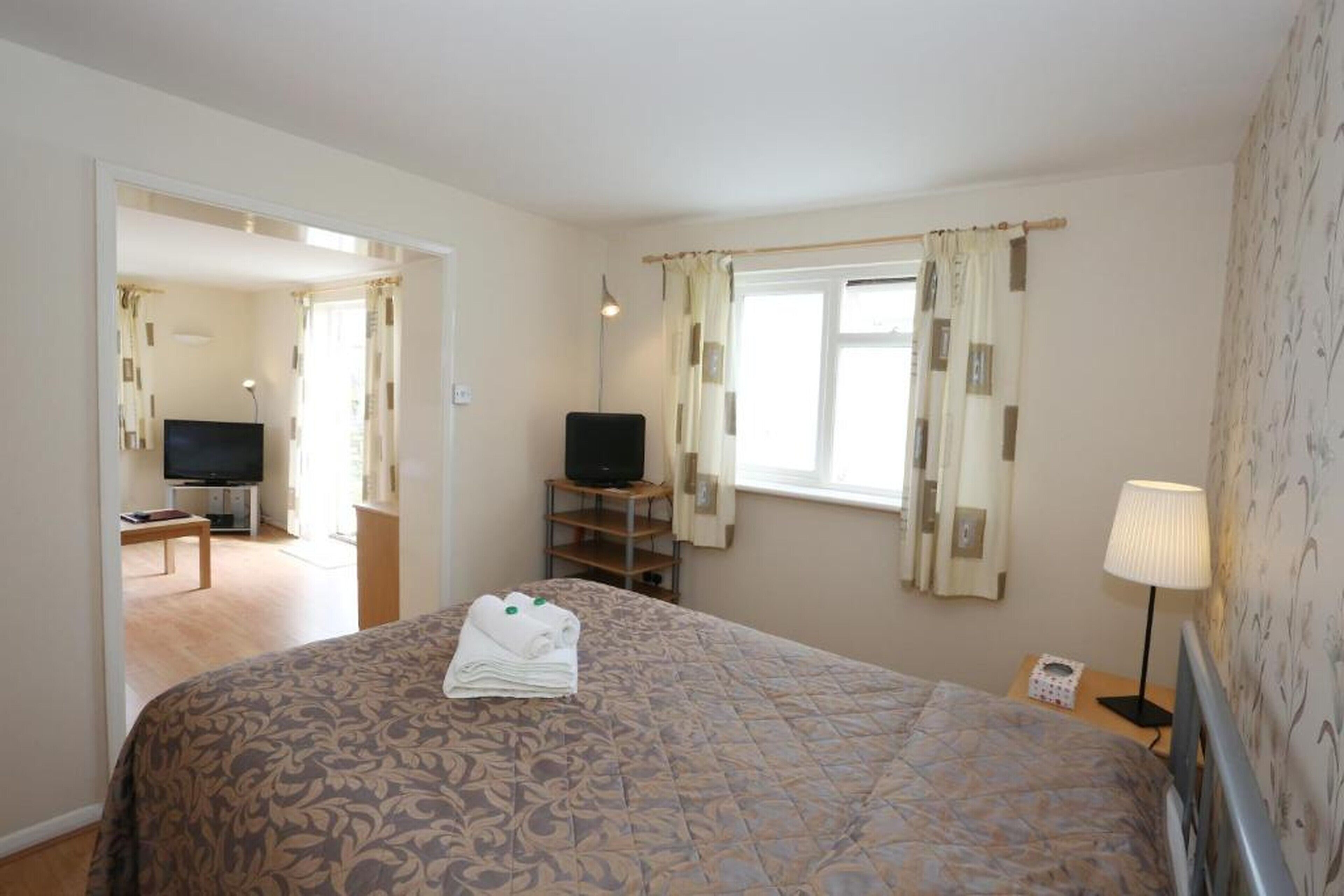 Una habitación de hotel con cama, televisor, escritorio y ventana con cortinas.