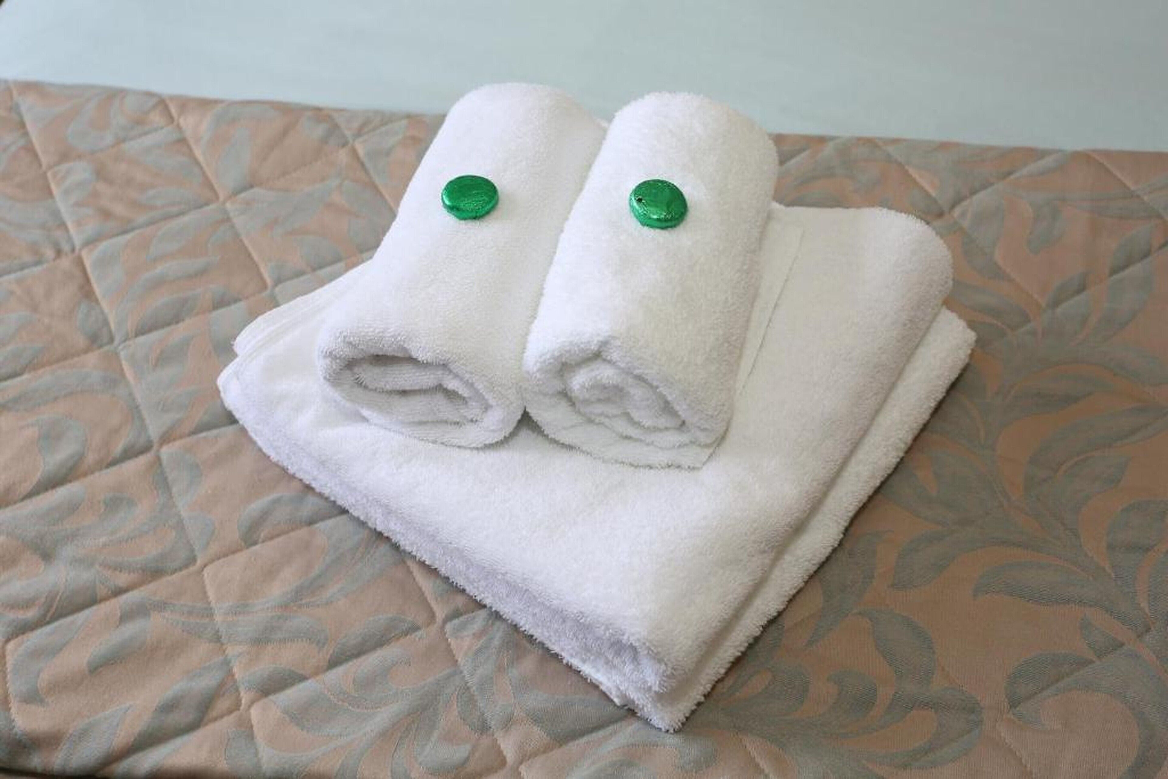 Two neatly folded white towels with green buttons on a bed with a patterned quilt.