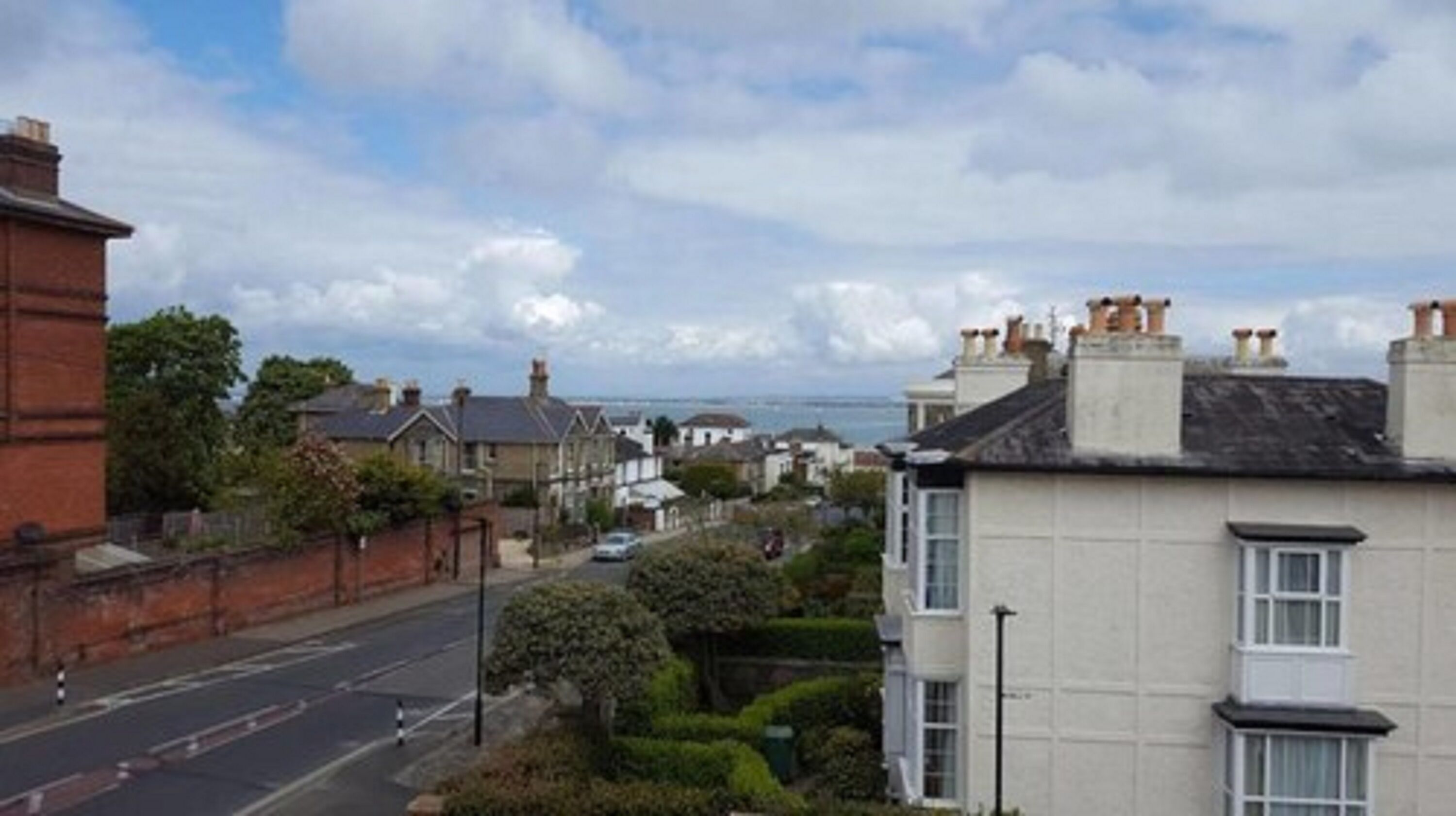 A residential street with houses, a clear sky, and a view of the sea.