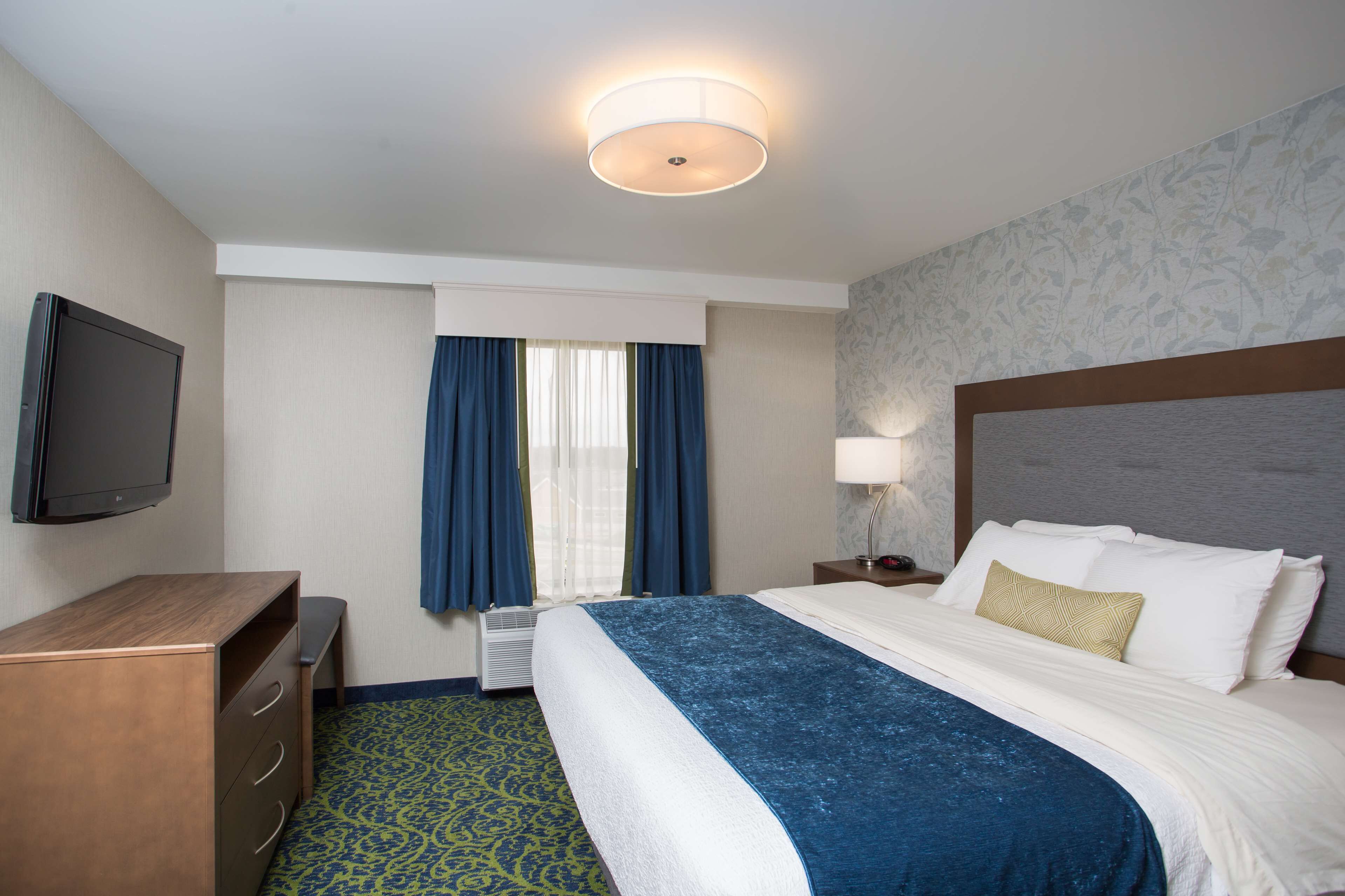 A hotel room with a bed, a desk, a television, and a window with curtains.