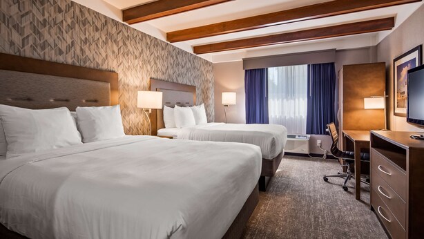 Habitación de hotel con dos camas, un escritorio, una silla, un televisor y un ventanal con cortinas.