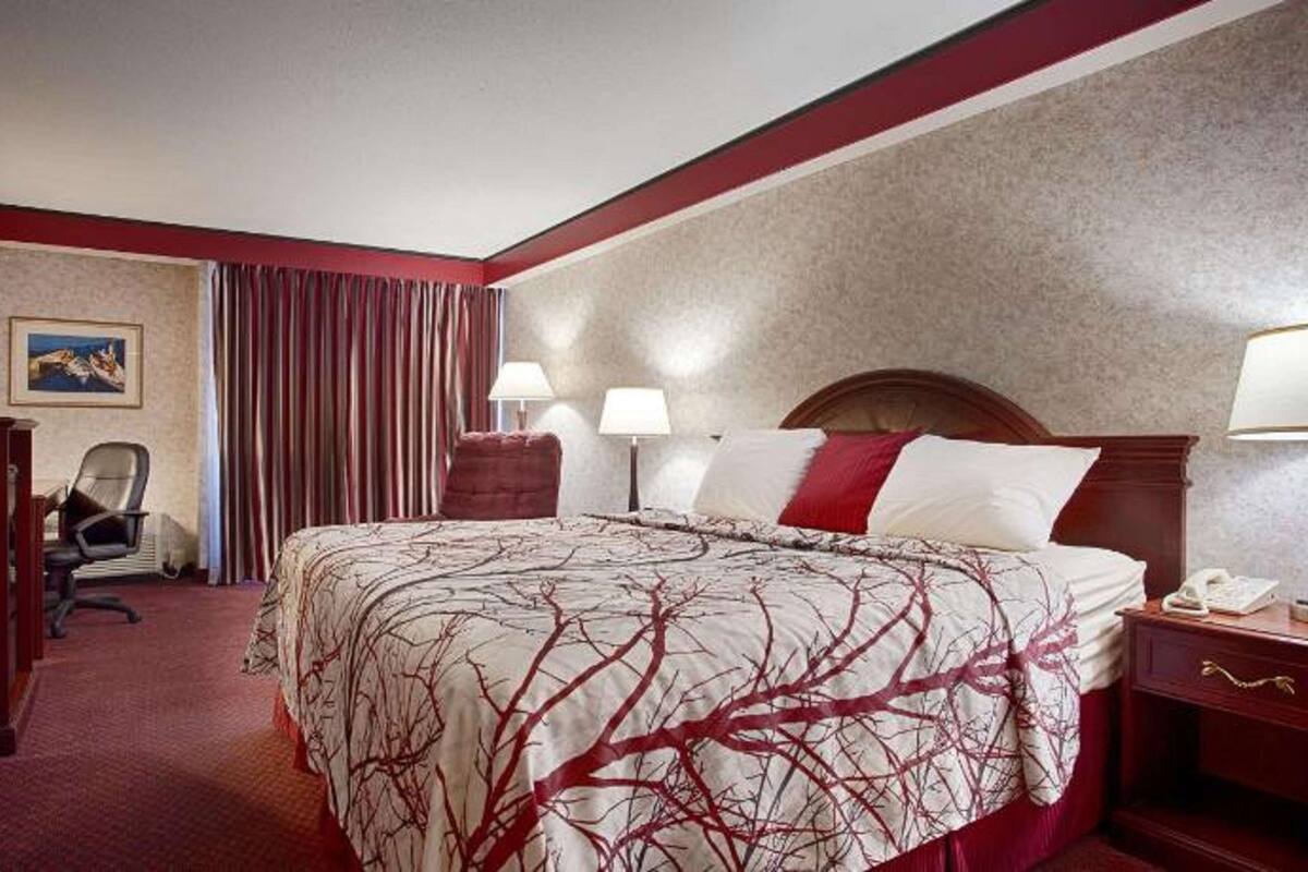 Una habitación de hotel con una cama grande, dos lámparas de noche, una mesita de madera, un escritorio con una silla y una cortina roja.
