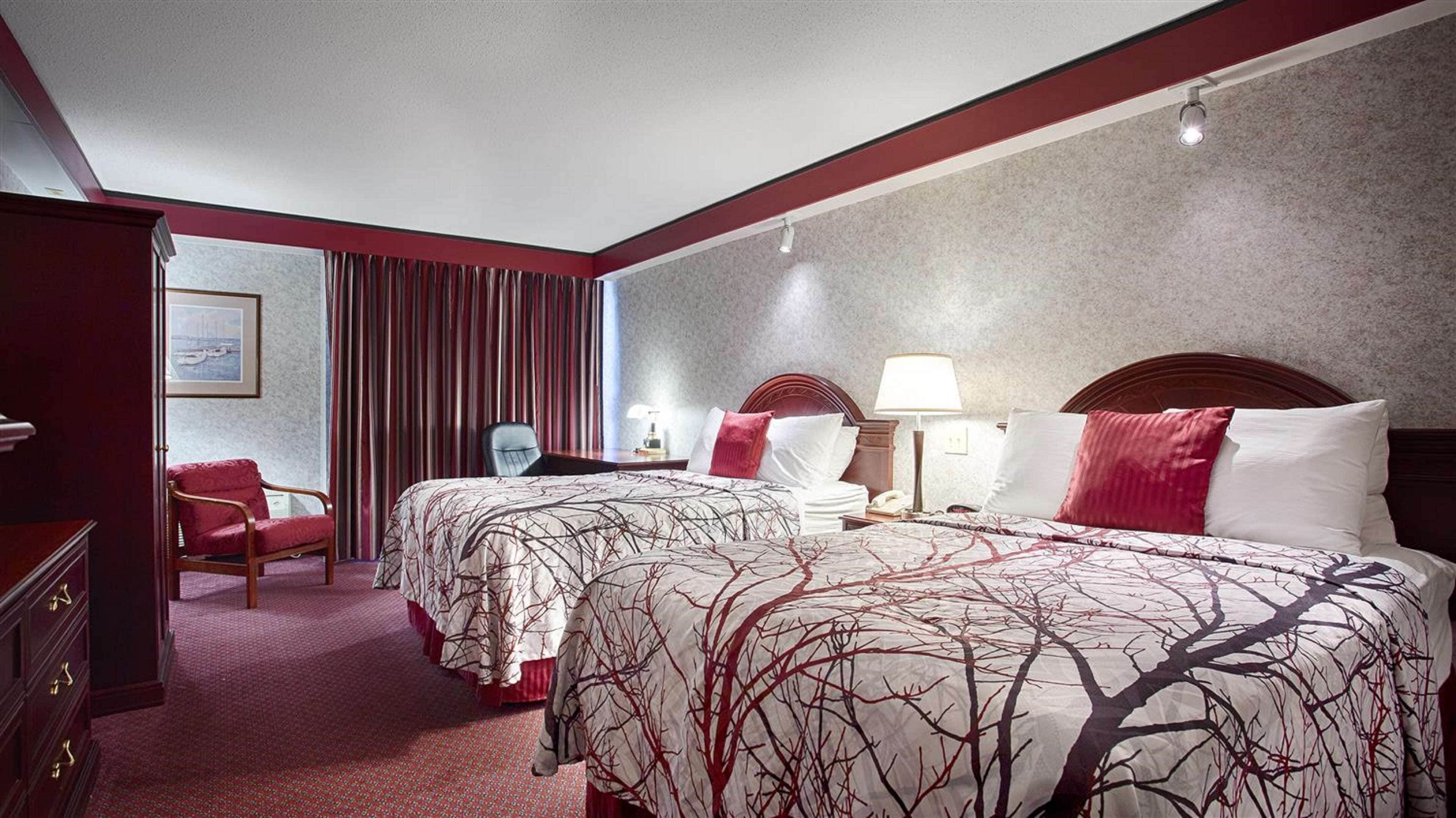 Une chambre d’hôtel avec deux lits, un bureau, une chaise et une fenêtre avec des rideaux.