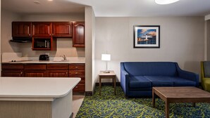 Una habitación de hotel compacta con kitchenette, un sofá azul, una mesita y una alfombra estampada.