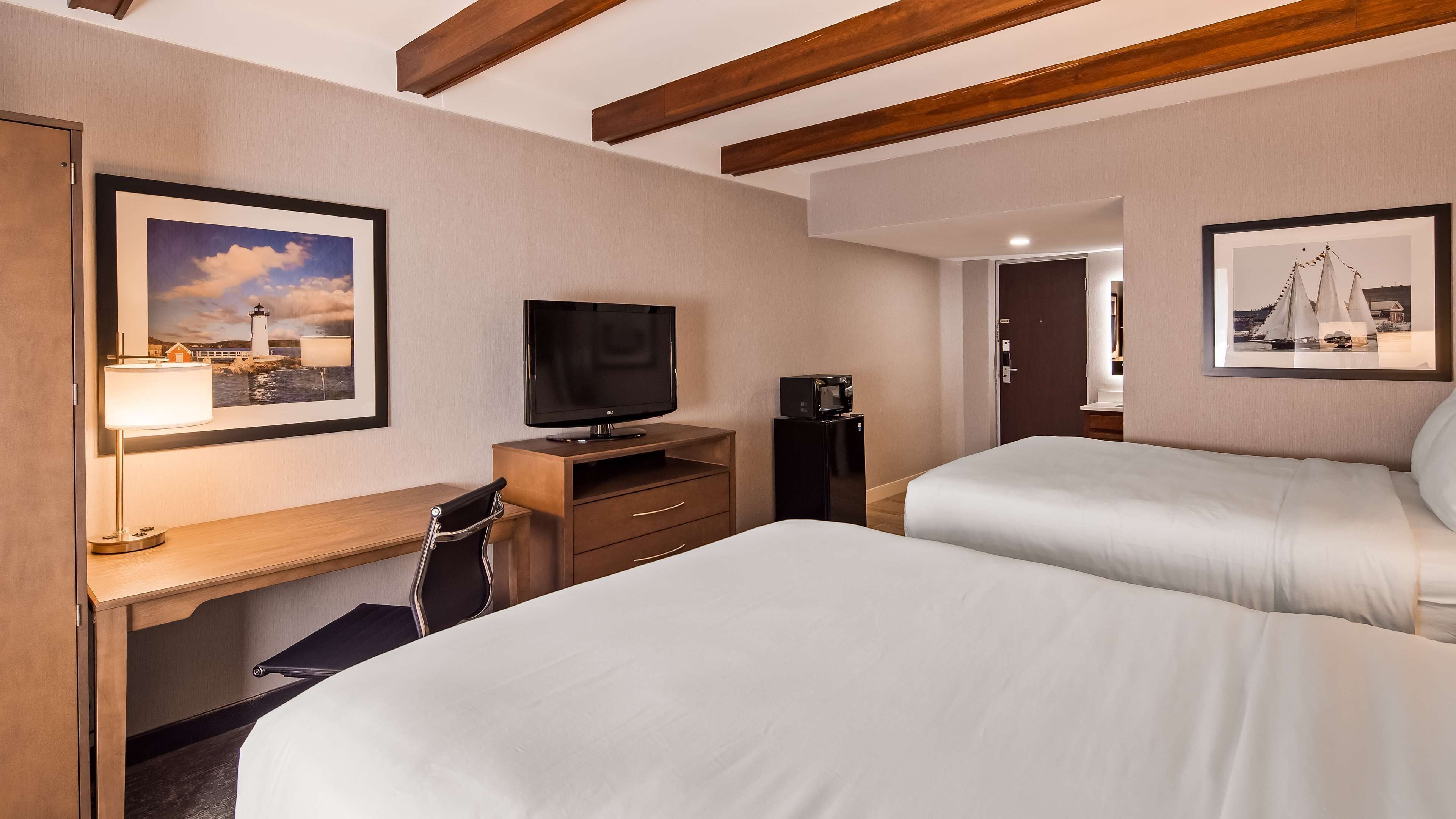 Een hotelkamer met twee bedden, een bureau met lamp, een televisie, een magnetron en beelden in lijsten aan de muur.