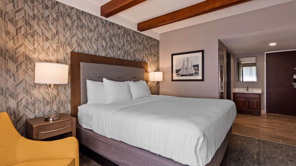 Habitación de hotel con una cama grande, dos lámparas de noche, un cabecero de madera, un cuadro enmarcado en la pared y un baño visible a través de una puerta abierta.
