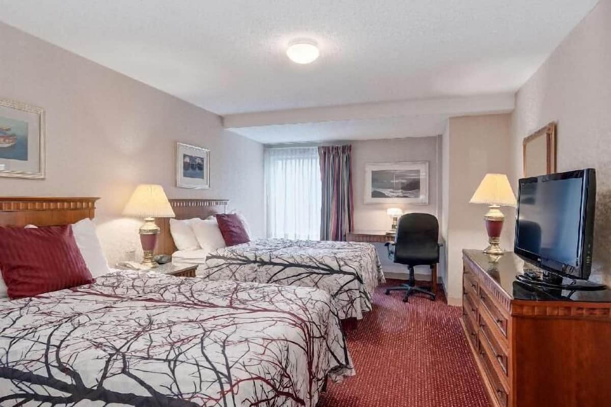 Habitación de hotel con dos camas, un escritorio, una silla, televisión y ventana con cortinas.