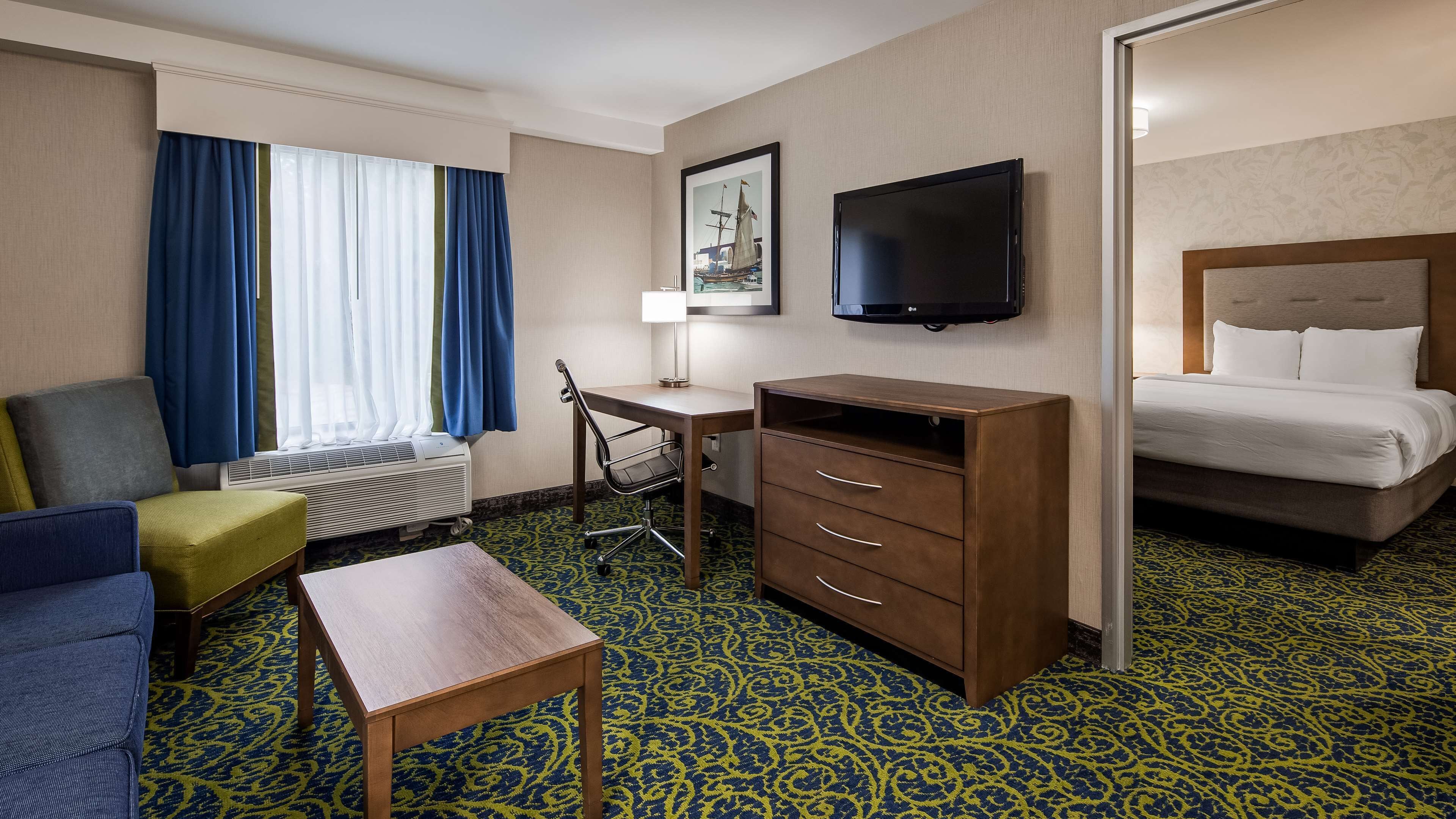Ein Hotelzimmer mit Bett, Schreibtisch, Stuhl, Fernseher und einem Fenster mit Vorhängen.