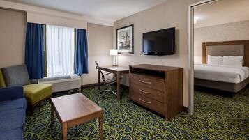 Une chambre d’hôtel avec un lit, un bureau, une chaise, une télévision et une fenêtre avec des rideaux.