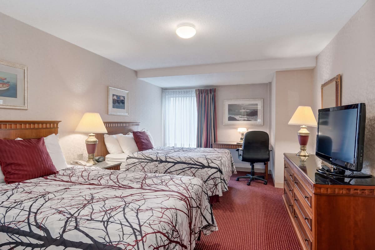 Habitación de hotel con dos camas, un escritorio, un televisor y una ventana con cortinas.