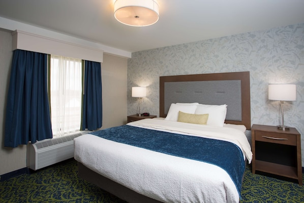 Una habitación de hotel con una cama grande, dos mesitas de noche con lámparas, un calefactor y una ventana con cortinas.