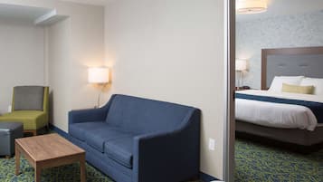 Una habitación de hotel con un sofá azul, una pequeña mesa de madera, un sillón verde y una cama con cabecera.