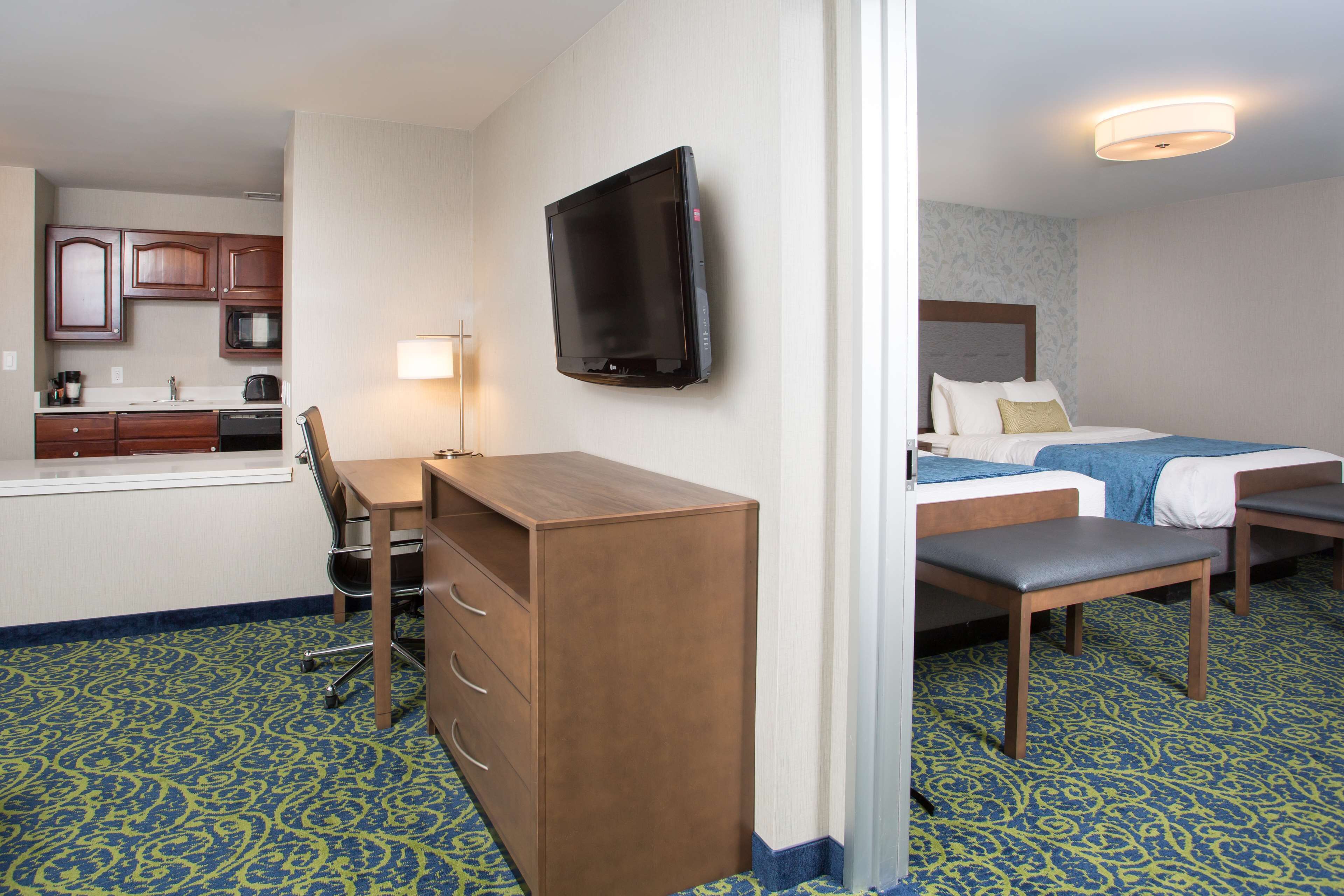 A hotel room with a kitchenette, a bed, a desk, and a television.